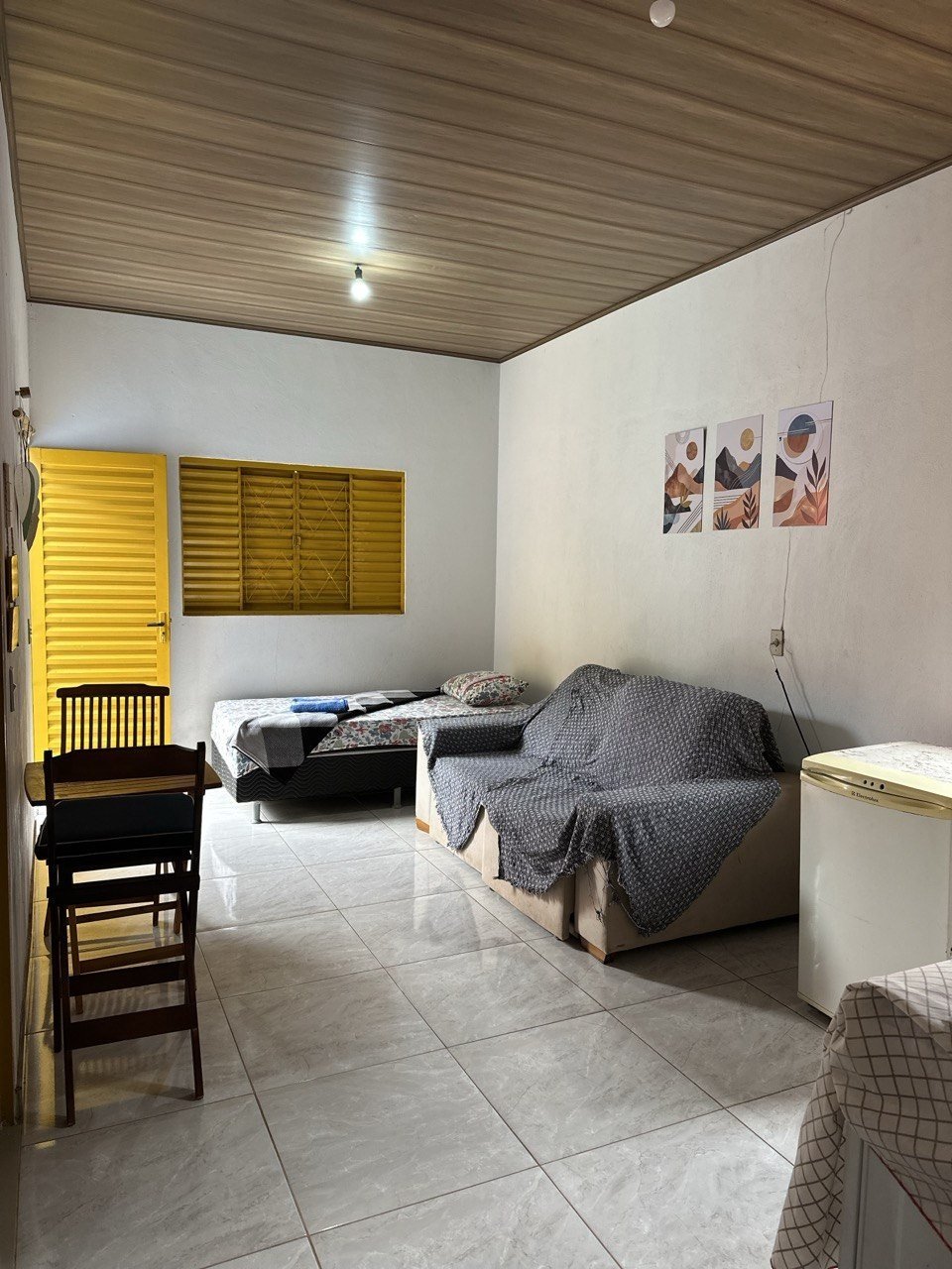 Sala do chalé com sofá, cama, mesa e porta de veneziana amarela